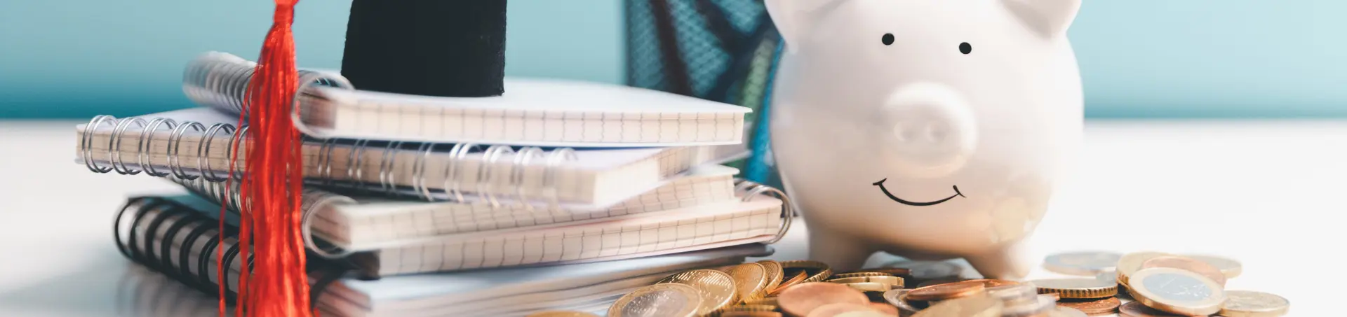 Libri scolastici e cappello da laurea accanto a un salvadanaio a forma di maialino e a monete, a rappresentare il rapporto tra istruzione, risparmio ed educazione finanziaria.