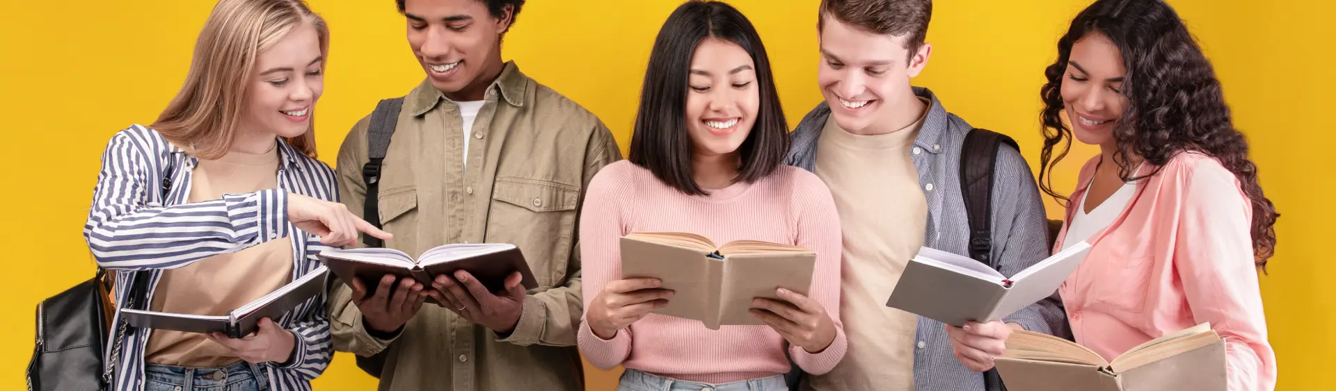 Gruppo multietnico di giovani ragazze e ragazzi sorridenti che leggono libri.